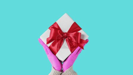Photo for Present delivery. Gift offering. Unrecognizable human hands in protective gloves holding wrapped box distancing congratulating isolated on blue free space background. - Royalty Free Image