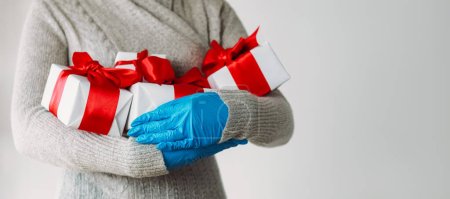 Photo for Virus present. Pandemic gift. Unrecognizable human hands in protective gloves embracing wrapped boxes isolated on gray copy space background. - Royalty Free Image