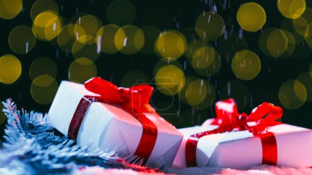 Foto de Vacaciones de invierno. Sorpresa de Navidad. Decoración festiva. Dos nuevas cajas de regalo de año envueltas en papel blanco con cinta roja en rama de pino luces de hadas de nieve desenfocadas fondo bokeh. - Imagen libre de derechos