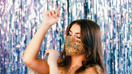 Photo for Quarantine fashion. Pandemic party dancing. Tender woman with festive makeup in matching creative luxury gold chain face mask on blur shiny tinsel background. - Royalty Free Image