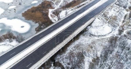 Photo for Drone winter bridge. Aerial frozen road. Beautiful countryside landscape with snowy lakes forest and asphalted government driveway. - Royalty Free Image