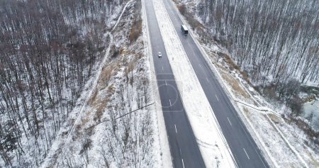Photo for Winter forest track. Aerial snowy road. Drone view of frozen asphalted traffic driveway through wood in cloudy cold morning. - Royalty Free Image