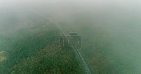 Photo for Drone road. Misty countryside. Nature scenery. Trees crowns and long asphalted way in fog on autumn cloudy dull day aerial view. - Royalty Free Image
