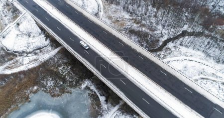 Photo for Drone snowy road. Aerial winter traffic. Countryside nature scenery with frozen lake with asphalted ice surface bridge cloudy day. - Royalty Free Image