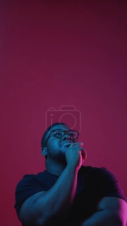 Photo for Making choice. Neon light portrait. Positive guy holding chin thinking over new ideas isolated on dark pink empty space background. - Royalty Free Image