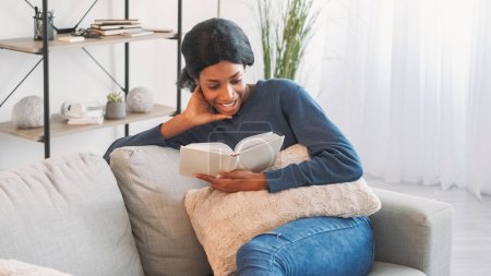 Photo for Book leisure. Indoors weekend. Smart delighted smiling young woman enjoying reading favorite bestseller story at home resting on couch in living room interior. - Royalty Free Image