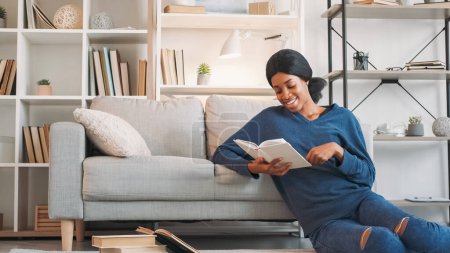Photo for Literature lifestyle. Favorite book. Young relaxed happy woman enjoying reading interesting novel story on floor at comfy sofa at home in living room free space. - Royalty Free Image