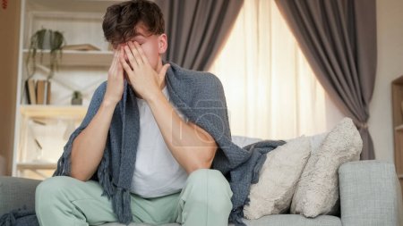 Photo for Migraine suffer. Exhausting pain. Feeling bad. Agony sick man with unbearable headache grasping head covered with plaid sitting on sofa at home. - Royalty Free Image