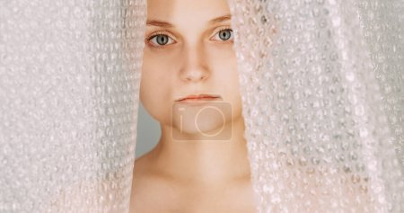 Photo for Plastic contamination. Polyethylene waste. Garbage recycling. Serious upset woman face portrait behind bubble wrap dangerous material packaging. - Royalty Free Image