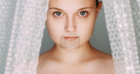Polyethylene disaster. Environmental pollution. Calm mindful woman portrait in textured cellophane bubble wrap film curtain on grey background.