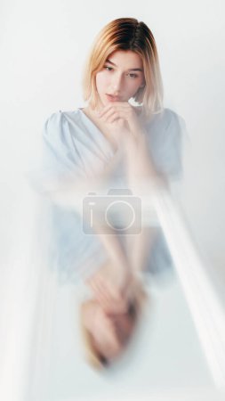 Photo for Bipolar disorder. Emotional crisis. Personality identity. Young thoughtful woman at defocused mirror reflection suffering from sickness on white background. - Royalty Free Image