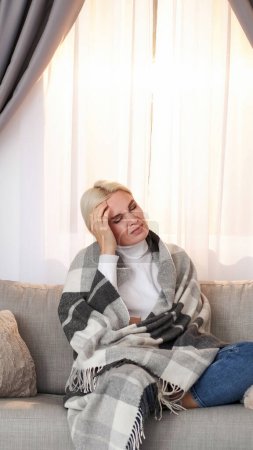 Foto de Dolor de cabeza. Sufrimiento frío. Mujer enferma infeliz con alta temperatura fatiga gripe síntomas dolorosos envueltos en manta descansando en el sofá en el espacio de copia en casa. - Imagen libre de derechos