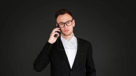 Photo for Business call. Mobile management. Corporate communication. Confident serious man in suit talking on phone discussing work isolated on dark black empty space background. - Royalty Free Image