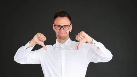 Photo for Dislike gesture. Negative feedback. Skeptic disappointed man rejecting with thumb down isolated on dark black copy space background. - Royalty Free Image