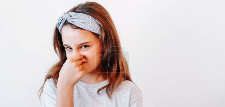 Disgusted child. Yuck kid. Dissatisfied picky naughty little girl pinching nose to avoid bad smell isolated on white copy space background.