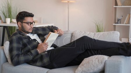 Photo for Reading book relax. Knowledge leisure. Home rest. Peaceful man student in glasses enjoying domestic weekend on comfy couch in cozy interior living room. - Royalty Free Image