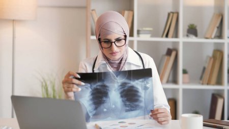 Photo for Radiology doctor. Medical diagnosis. Professional healthcare. Serious woman physician examining lung pneumonia x-ray film at hospital workspace. - Royalty Free Image