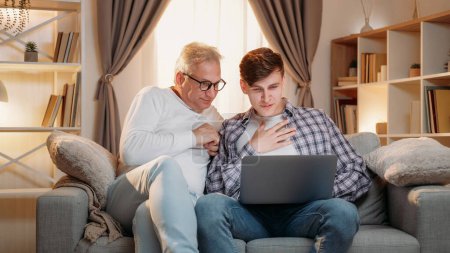 Internet leisure. Family generation. Online research. Happy inspired father and son surfing on laptop together home room interior.