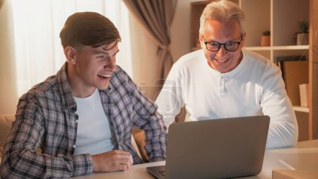 Family leisure. Internet bidding. Online auction. Happy father and son watching football sport game together at laptop home interior.