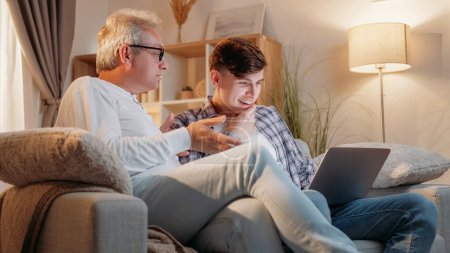 Vater-Sohn-Freizeit. Familienruhe. Digitales Leben. Senior-Papa und neugieriger Nachwuchs diskutieren im Internet über Laptop-Home-Room.