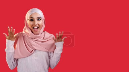 Téléchargez les photos : Gagnante wow. La surprise de la victoire. Opportunité passionnante. Étonné étonné ravi femme heureuse dans hijab isolé sur fond d'espace vide rouge. - en image libre de droit