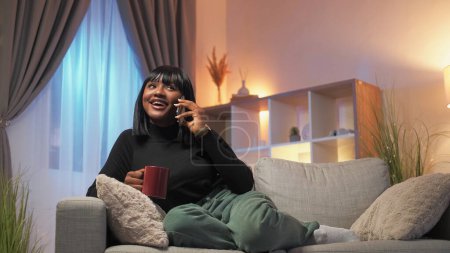 Mobile talk. Relaxed woman. Home leisure. Happy smiling female enjoying phone communication sitting sofa cozy living room interior.