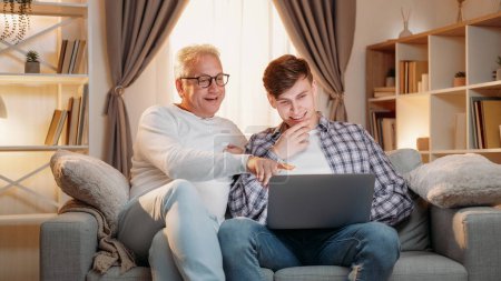 Photo for Internet booking. Family research. Online payment. Happy inspired father and son choosing holiday tickets on laptop together home room interior. - Royalty Free Image