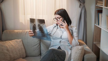 Photo for Lung diagnosis. Working physician. Medical healthcare. Serious woman examining x-ray film consulting patient on phone about pneumonia at hospital. - Royalty Free Image