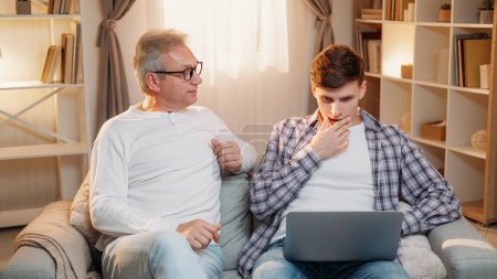 Photo for Parent teaching. Family support. Senior father helping puzzled son in using work program online on laptop light home room interior. - Royalty Free Image
