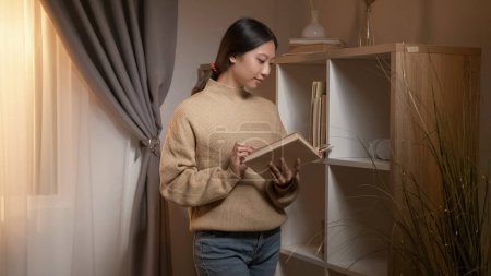 Lectura casera. Estudia inspiración. Literatura de fin de semana. Mujer inteligente disfrutando de aprender a escoger libros desde el estante en el interior de la habitación.