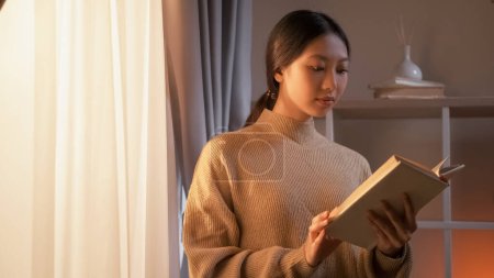 Photo for Home learning. Knowledge wisdom. Intelligent pensive woman enjoying reading book staying near window in light room interior. - Royalty Free Image