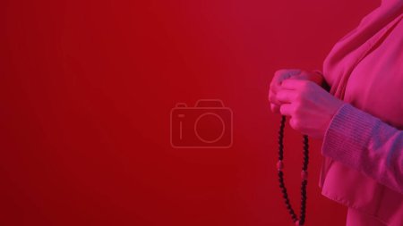 Photo for Wooden rosary. Ramadan pray. Unrecognizable woman praying with tasbih beads in hands in neon light on red copy space background. - Royalty Free Image