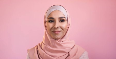 Islamic woman portrait. Muslim beauty. Happy confident smiling pretty female face in hijab headscarf isolated on pink empty space background.
