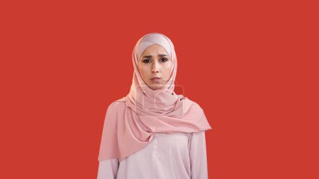 Scared woman. Fear anxiety. Stress problem. Disturbed shocked frightened female face in hijab with open mouth isolated on red copy space background.