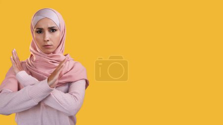 Stopp-Geste. Weiblicher Protest. Gestörte strenge Frau im Hijab zeigt gekreuzte Hände Uneinigkeit isoliert auf gelbem Leerraum Hintergrund.