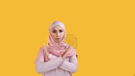 Pas de geste. Arrêtez le rejet. Refuser la réaction. Femme préoccupée dans le hijab montrant refus mains croisées isolé sur fond d'espace vide orange.