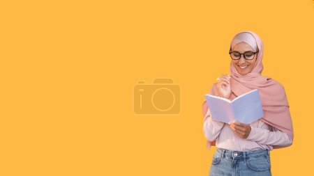 Escribiendo hobby. Estudia inspiración. Mujer inteligente sonriente curiosa pensativa en gafas de hijab con bolígrafo tomando notas en diario aislado sobre fondo de espacio vacío naranja.