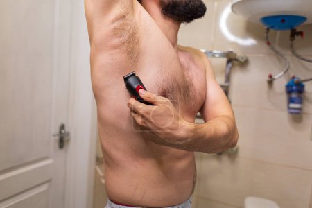 Man shaves his armpits. A man with an athletic figure in the bathroom.