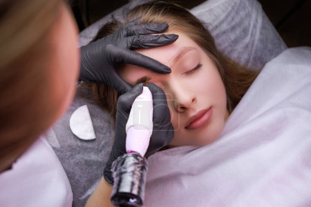 Photo for In the hands of the master tattoo machine he applies permanent makeup on the eyebrows. PMU Procedure, Permanent Eyebrow Makeup. - Royalty Free Image