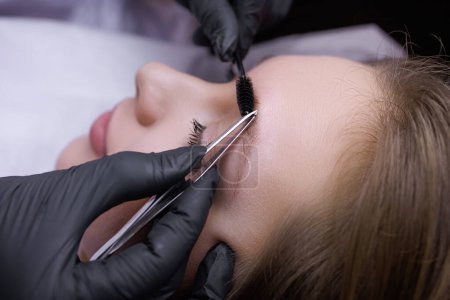 Photo for Plucking the eyebrows along the contour with tweezers before the permanent makeup procedure. PMU Procedure, Permanent Eyebrow Makeup. - Royalty Free Image