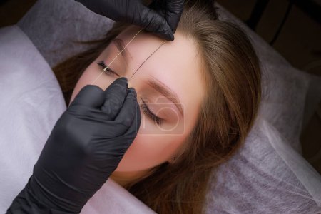 Photo for Before the permanent makeup procedure, the master makes a marking with a thread on the model's eyebrows. PMU Procedure, Permanent Eyebrow Makeup. - Royalty Free Image