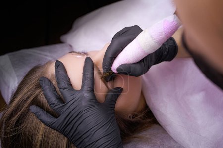 Photo for Applying permanent makeup on the eyebrows with a tattoo machine held by a master in black gloves. PMU Procedure, Permanent Eyebrow Makeup. - Royalty Free Image