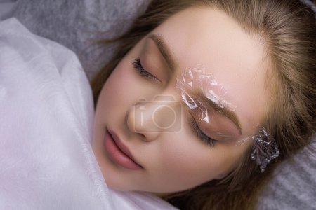 Photo for Anesthesia is applied to the model's eyebrow and the eyebrow is covered with a transparent film. PMU Procedure, Permanent Eyebrow Makeup. - Royalty Free Image
