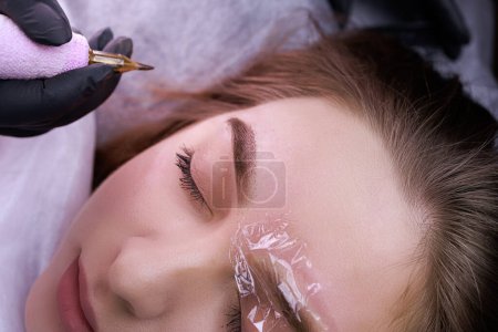 Photo for Applying permanent makeup to the model's eyebrow while the other eyebrow is under anesthesia. PMU Procedure, Permanent Eyebrow Makeup. - Royalty Free Image