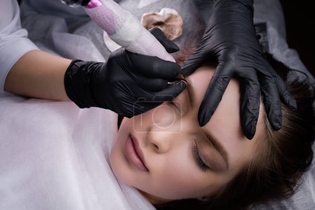 Technique of air application of permanent makeup on the model's eyebrows. PMU Procedure, Permanent Eyebrow Makeup.