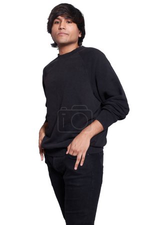 Photo for A young man in his 20s posing for the camera, he is wearing a black T-shirt and black jeans. He is standing with his two hands in his pocket. Serious look, self-confident. - Royalty Free Image