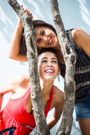 Photo for Portrait of two girls between a tree branch against a light blue wall. City girls far from the capital. - Royalty Free Image