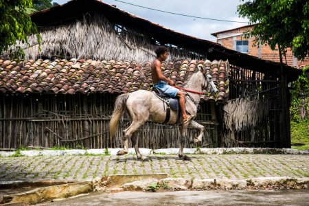 Téléchargez les photos : Aratuipe, Bahia, Brésil - 31 août 2018 : Un jeune homme à cheval passe devant une façade d'un magasin de céramique dans la ville d'Aratuipe, Bahia. - en image libre de droit