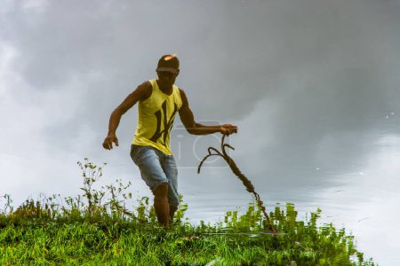 Téléchargez les photos : Aratuipe, Bahia, Brésil - 31 août 2018 : Réflexion dans l'eau d'un homme tirant une corde sur la rive de la rivière Jaguaripe dans la ville d'Aratuipe, Bahia. - en image libre de droit