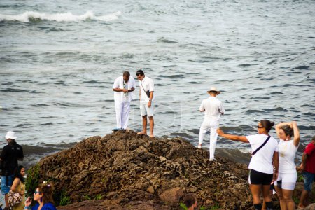Téléchargez les photos : Salvador, Bahia, Brésil - 02 février 2023 : Des gens sont vus au sommet des rochers à la plage de Rio Vermelho, offrant des cadeaux à Yemanja, à Salvador, Bahia. - en image libre de droit